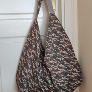 Bolso Origami Camuflaje de loneta de algodón 100% confeccionado al estilo origami, estampado tipo camuflaje de tonos verdes y marrones, estructura geométrica de una sola pieza con asa ancha integrada colgado de un pomo.